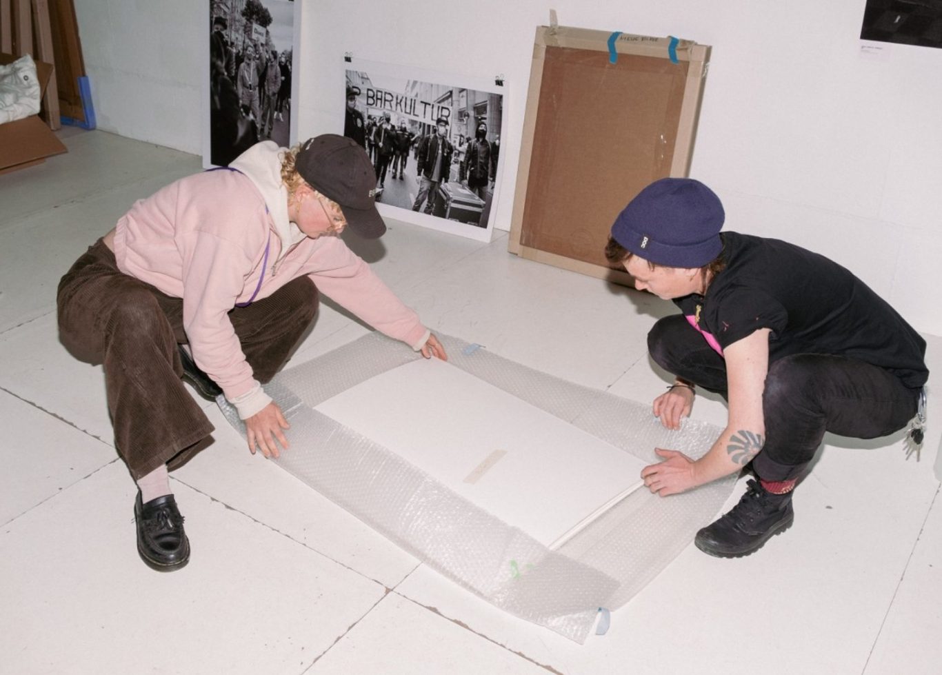 Srufio Fräns & Nietze Kollektiv WERT @ Galerie KUB Leipzig © Anna Luisa Richter Zwei Personen legen ein großes Blatt Papier auf den Boden in einem kreativen Raum.